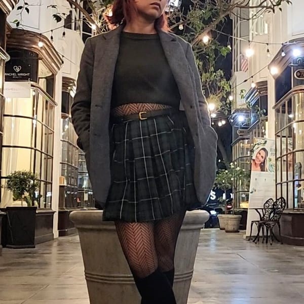 Model posed standing wearing cropped sweater, plaid skirt, herringbone tights, knee high socks, and boots with a blazer